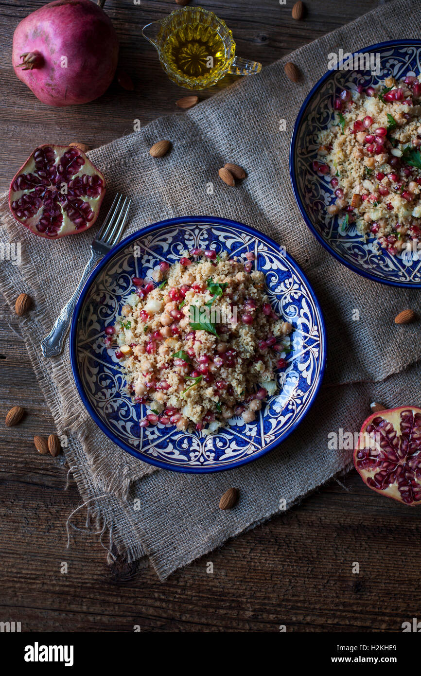 Couscous with chickpeas, almonds and pomegranate on ceramic blue plates and rustic wooden table Stock Photo