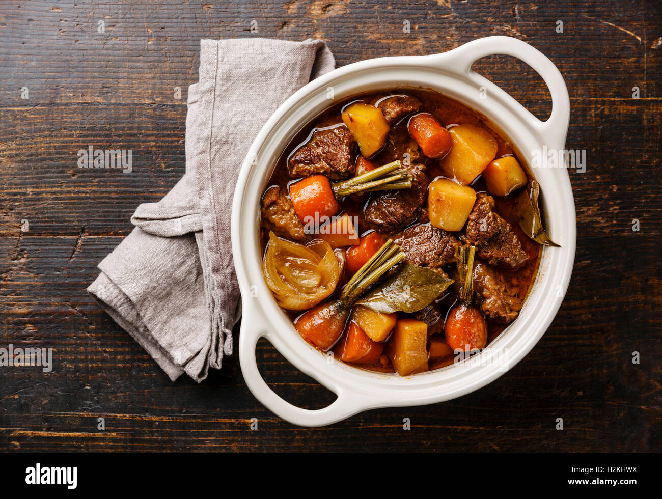 Beef meat stewed with potatoes, carrots and spices in ceramic pot on wooden background Stock Photo