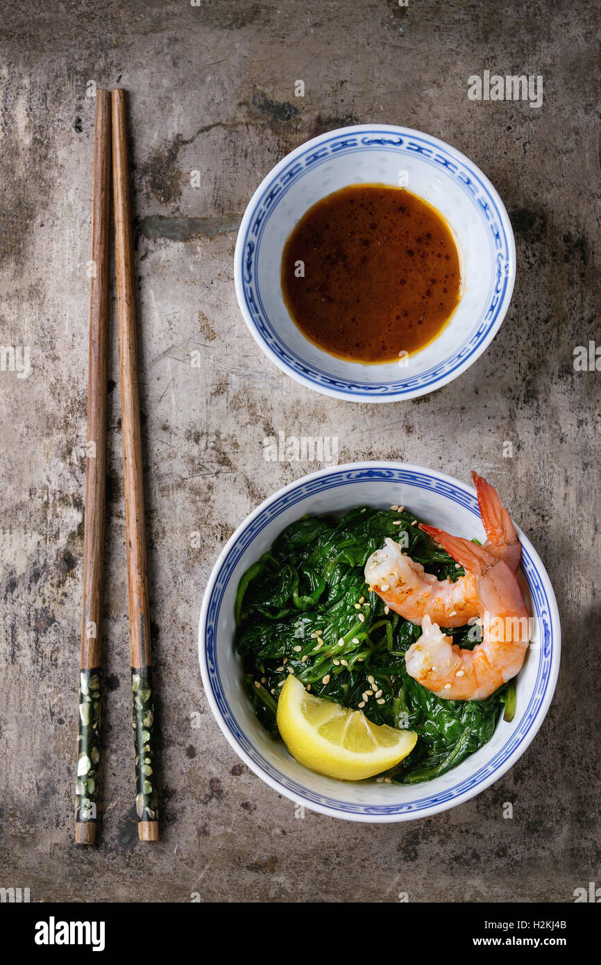 Chinese bowls with Cooked spinach and fried shrimps prawns with lemon and sesame seeds, soy sauce and chopsticks over old iron b Stock Photo