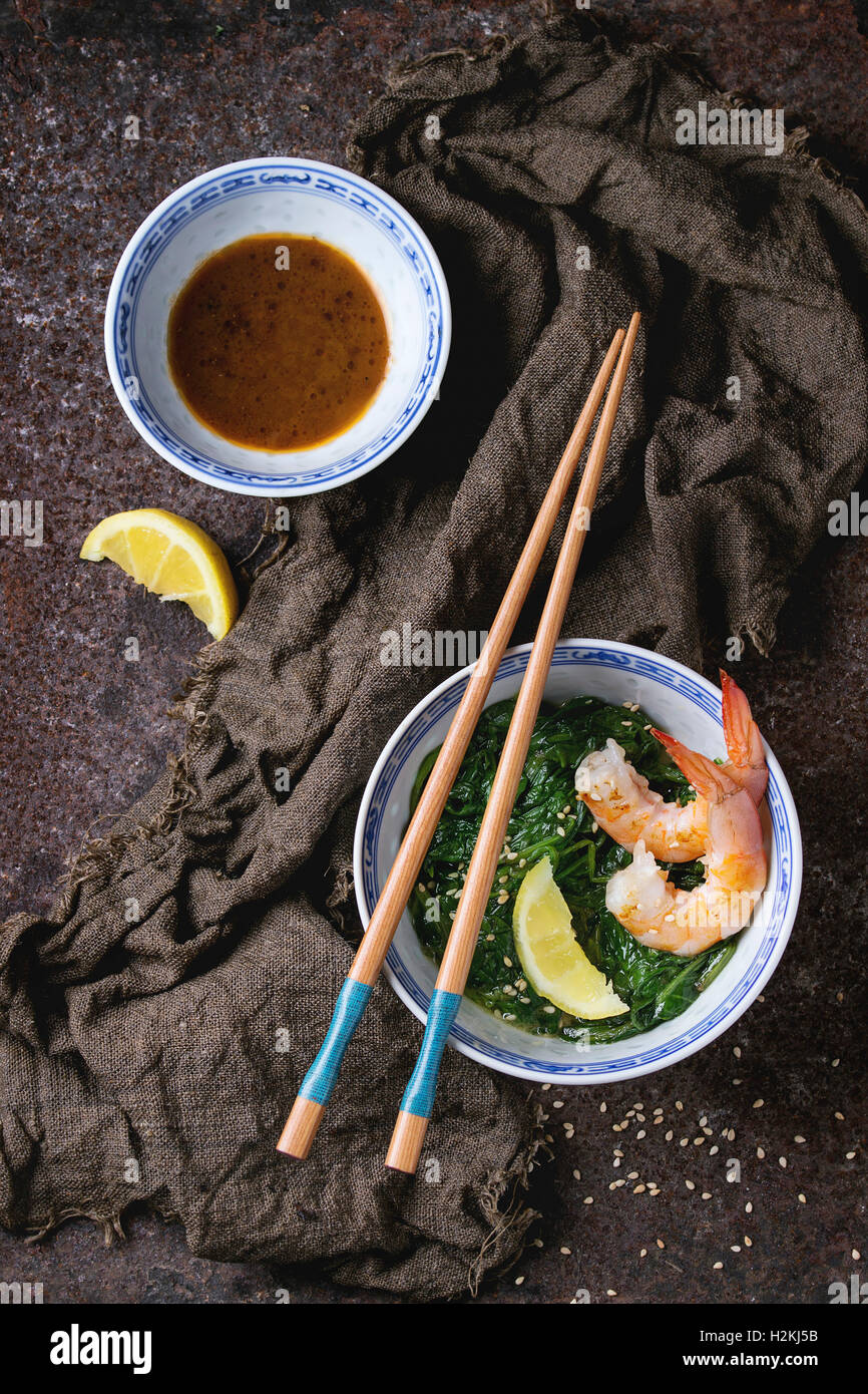 Chinese bowls with Cooked spinach and fried shrimps prawns with lemon and sesame seeds, soy sauce and chopsticks on sackcloth ov Stock Photo