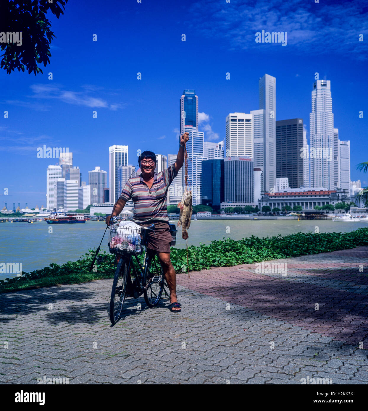 Angler with bike holding a fish in front of Central business district skyline with skyscrapers, Marina Bay, Singapore Stock Photo