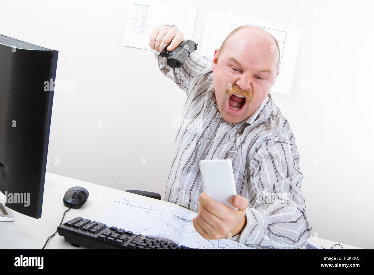 Angry Businessman Aiming Gun On Mobile Phone At Desk Stock Photo