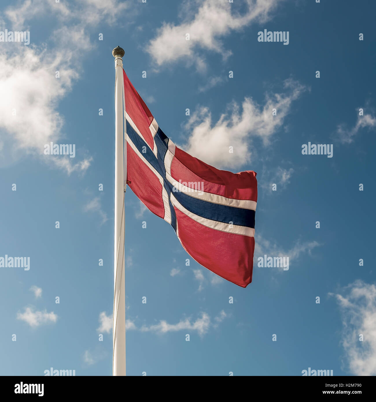 A Norwegian flag flutters in the wind against a blue sky background Stock Photo
