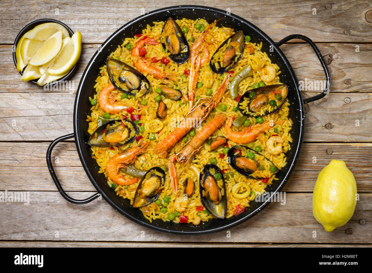 Spanish paella on a wooden table with lemon on a bowl and a fresh lemon Stock Photo