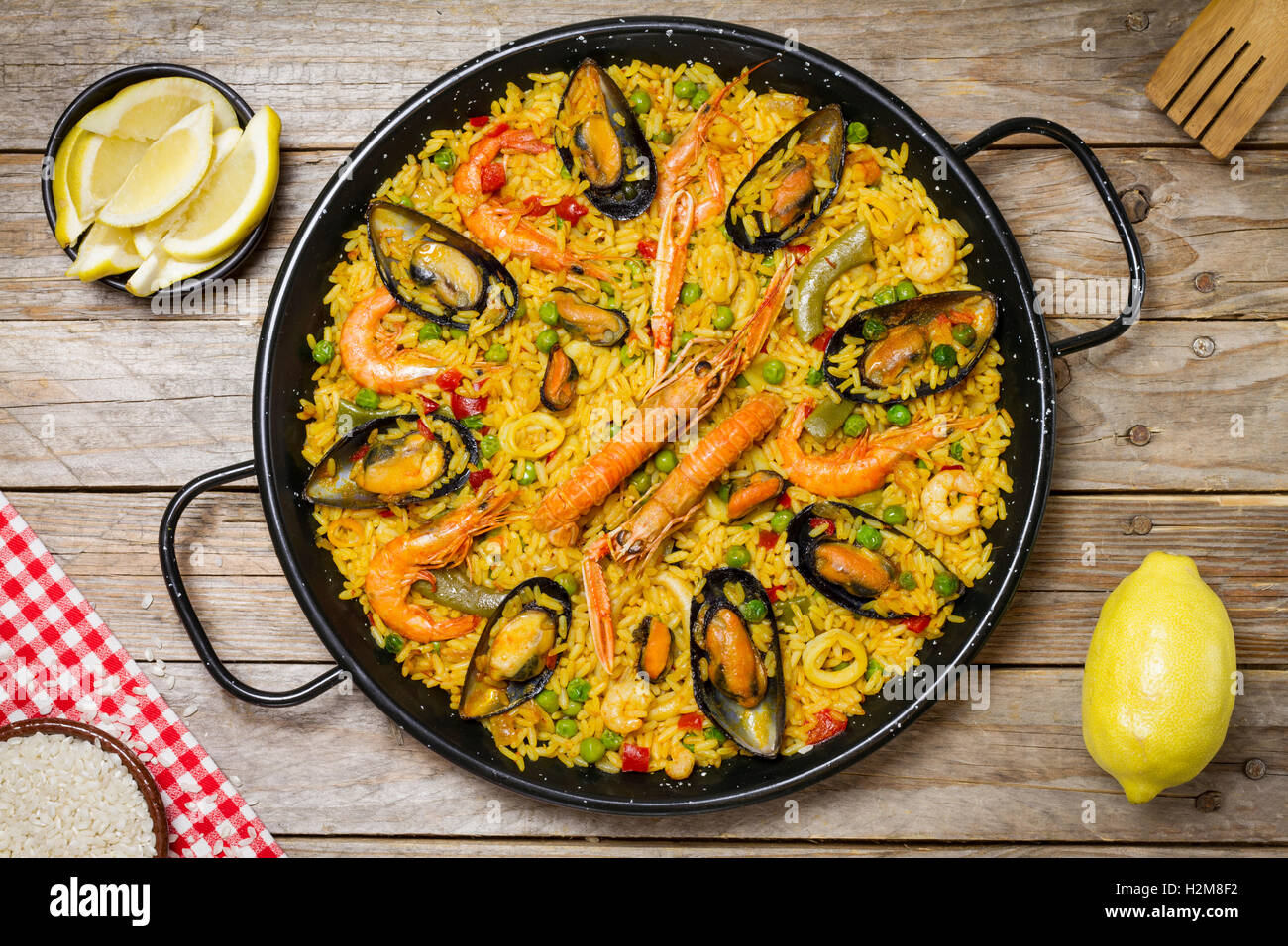 Spanish paella on a wooden table with fresh lemon and a white and red tablecloth and a wooden fork Stock Photo