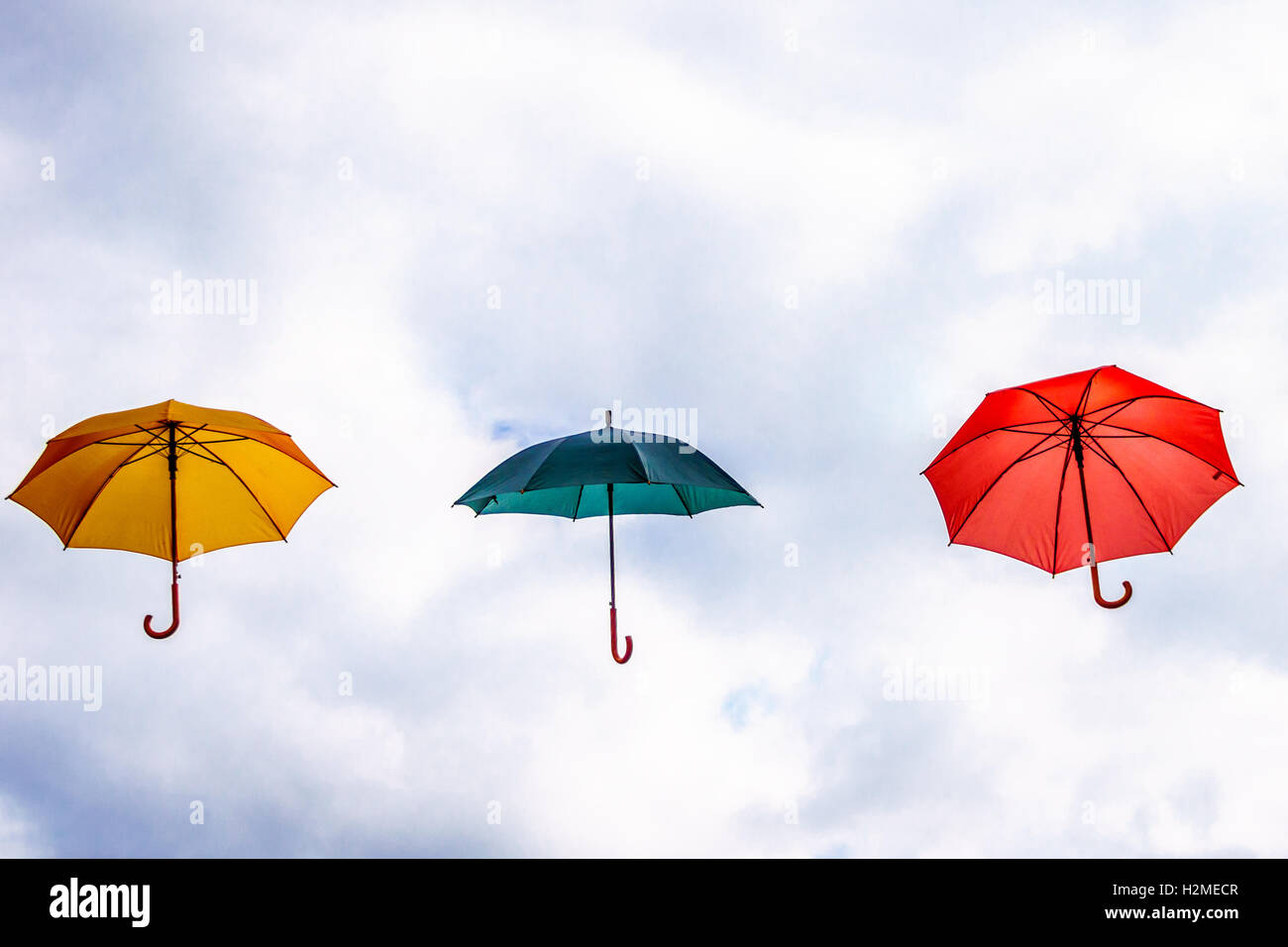 Yellow Umbrella, Green Umbrella, Red Umbrella floating in the Air under Partly Blue Sky with cloudy periods. Stock Photo