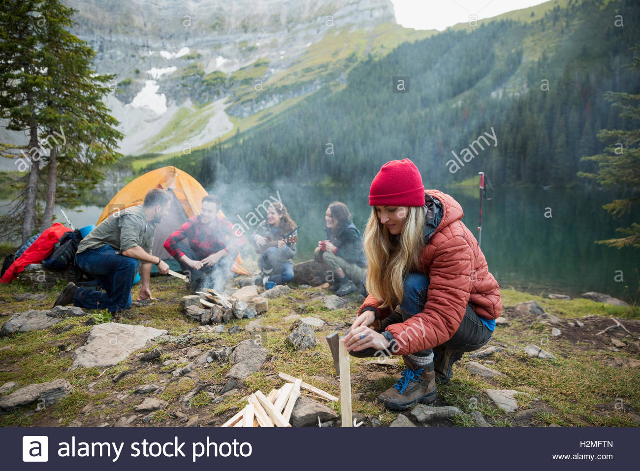 Woman splitting firewood at remote lakeside campsite Stock Photo