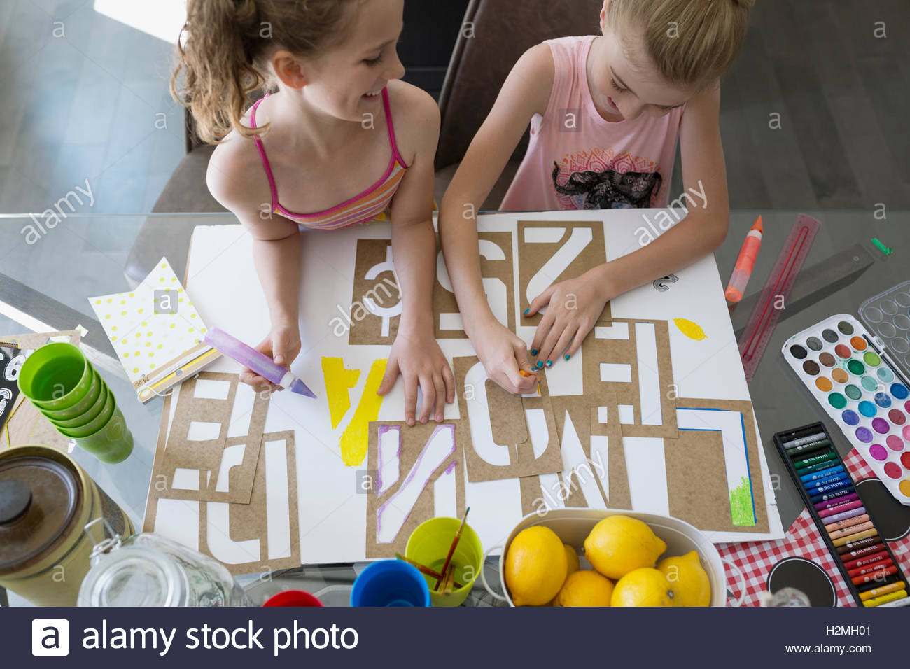 Girls making lemonade sign with stencils at dining table Stock Photo