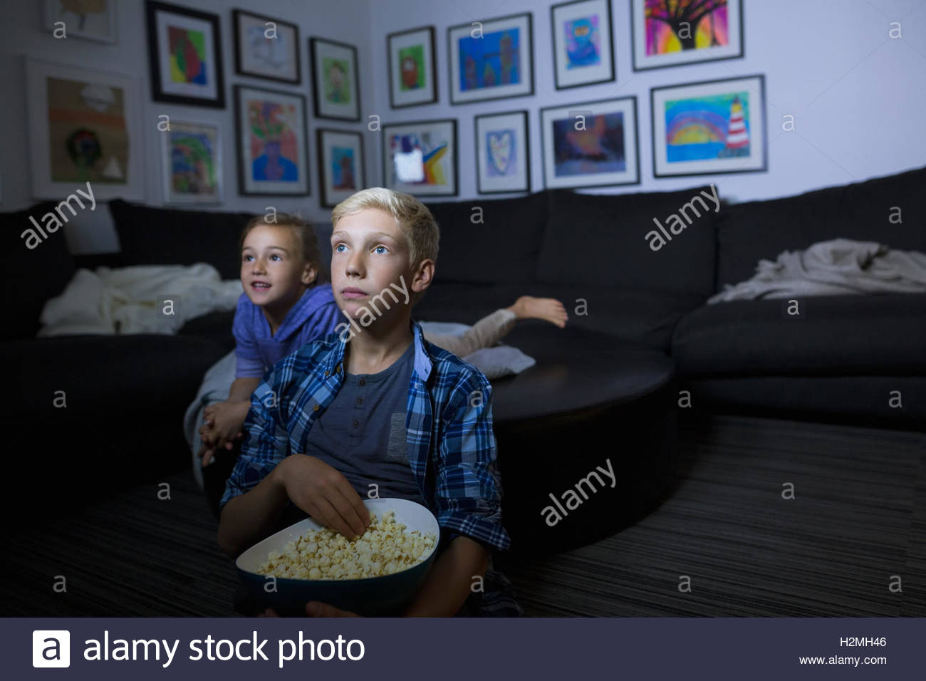 Brother and sister eating popcorn watching movie in dark living room