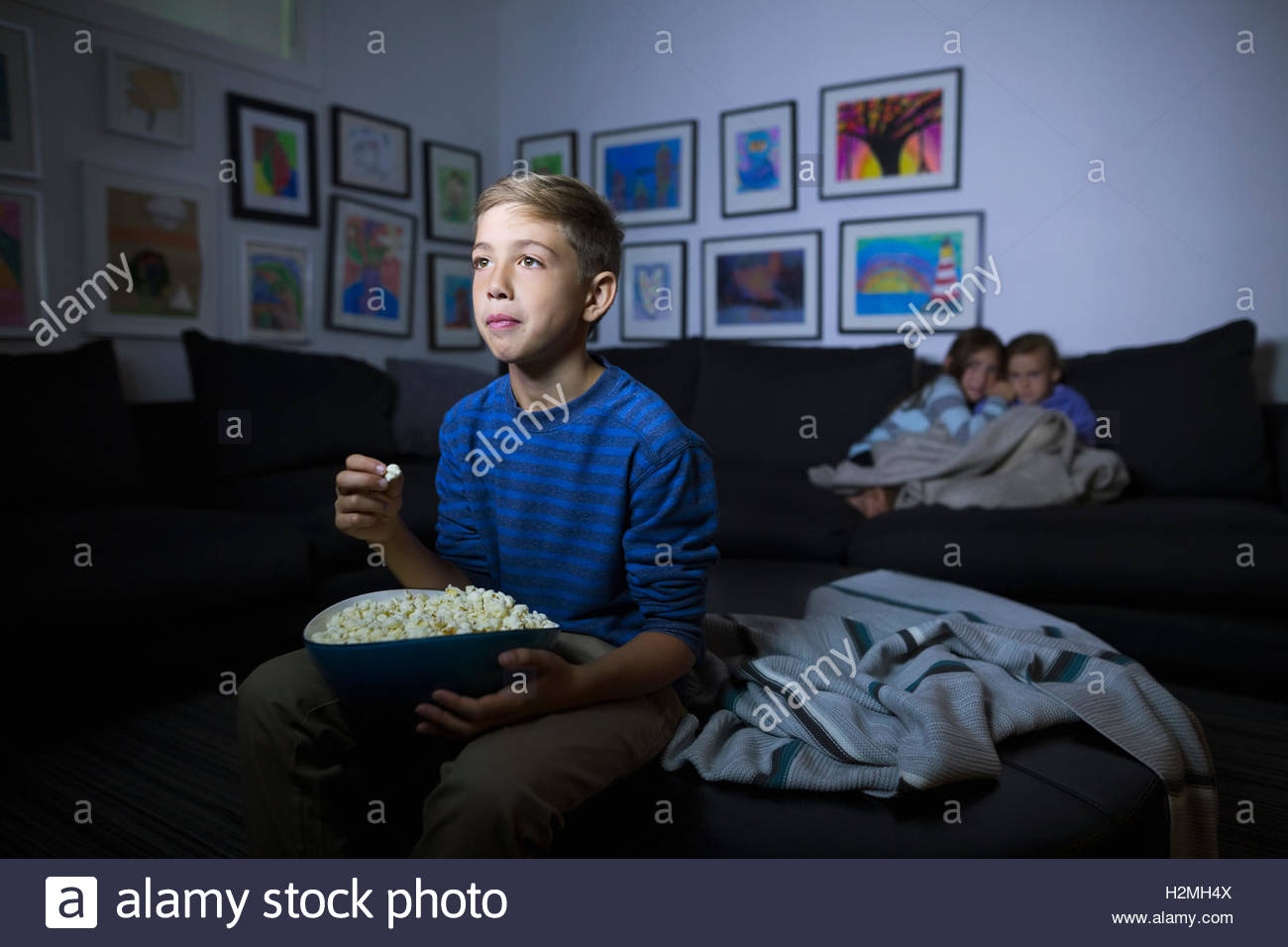 Brother and sisters eating popcorn watching movie in dark living room