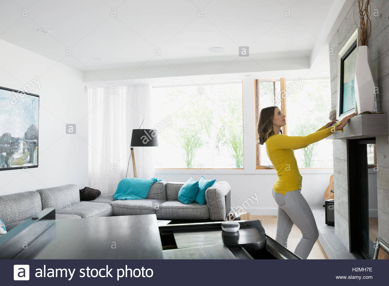 Young Woman Hanging Painting Over Fireplace In Living Room Stock