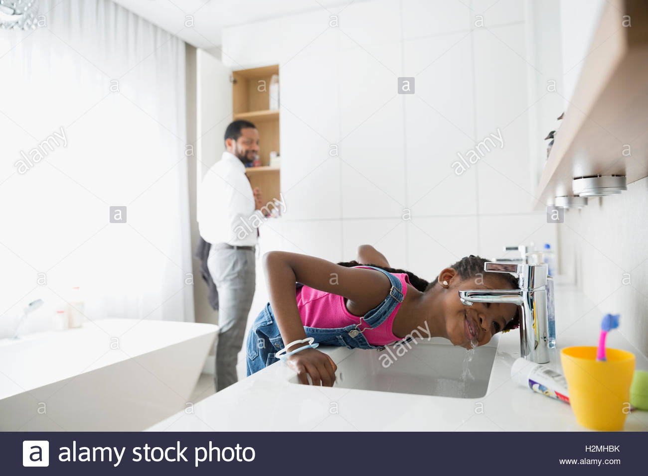 Father watching daughter sipping water from faucet in bathroom Stock Photo
