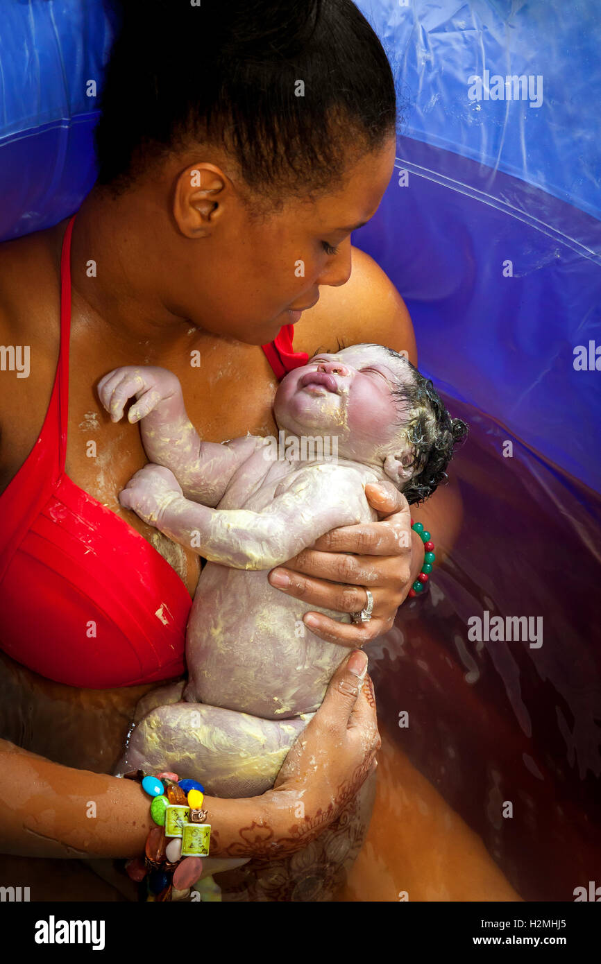 A beautiful, African American woman cradles her newborn daughter in a birthing pool moments after delivering her at home. Stock Photo
