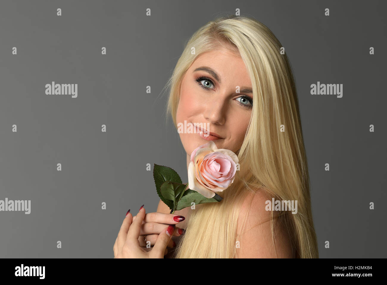 Portrait of young woman holding pink rose isolated over gray background Stock Photo