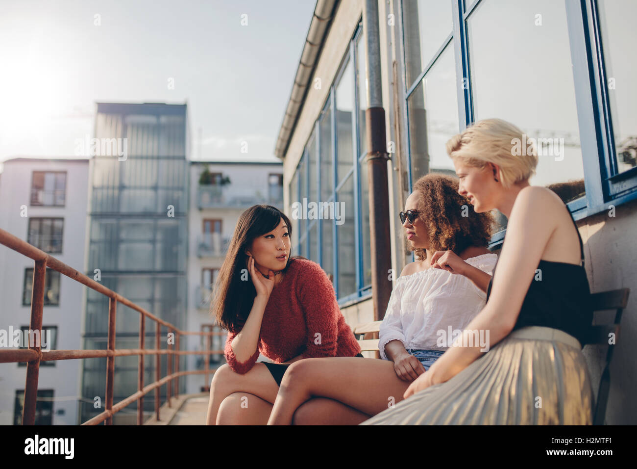 Three young women sitting outdoors and chatting. Multiracial group of females relaxing in terrace. Stock Photo