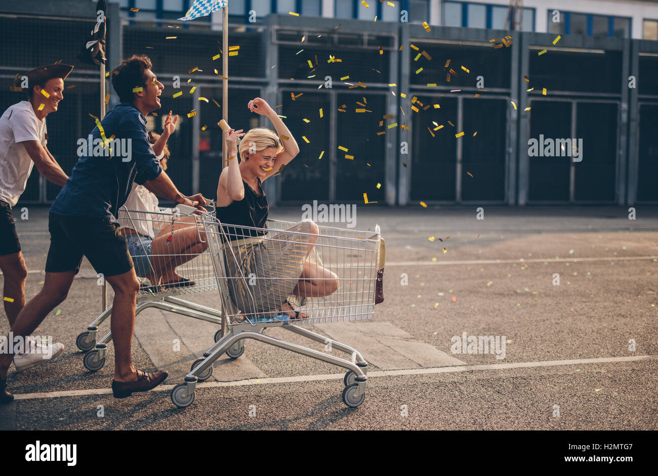 Multiethnic young people racing with shopping cart and blowing confetti