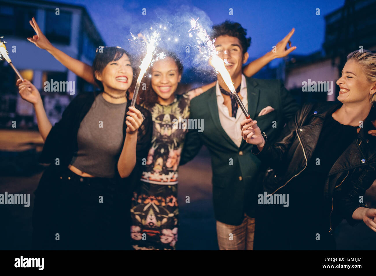 Group of friends holding sparklers out on street at night. Young men and women having night party with sparklers. Stock Photo