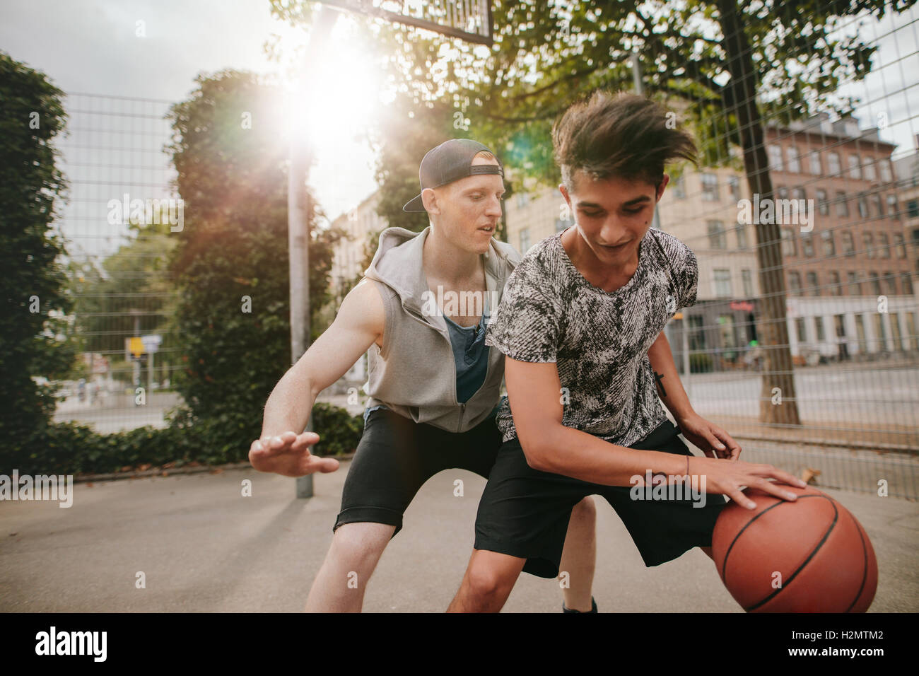 Young man dribbling basketball with friend blocking. Friends playing basketball on outdoor court and having fun. Stock Photo