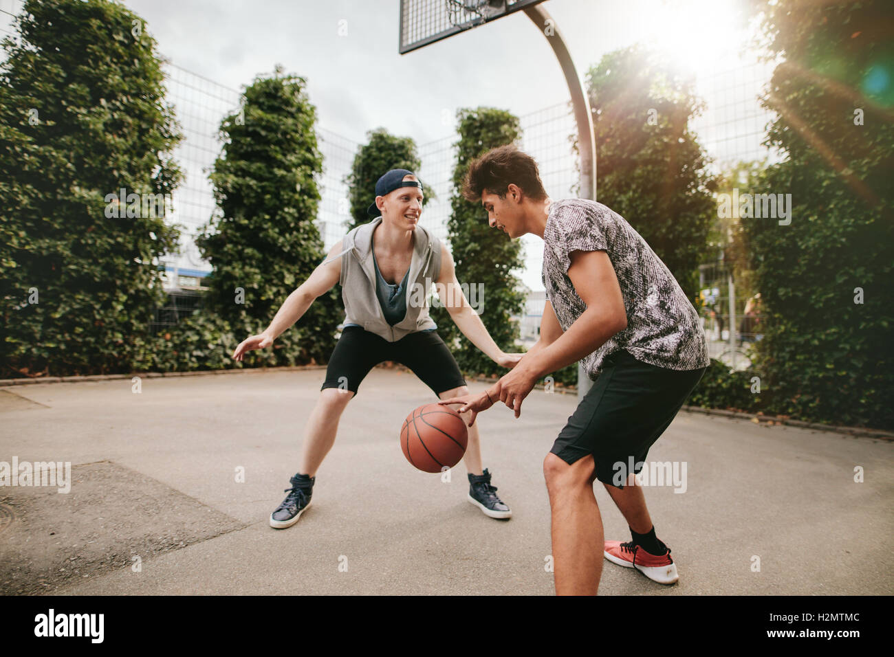 Teenagers playing basketball on outdoor court and having fun. Young man dribbling basketball with friend blocking. Stock Photo