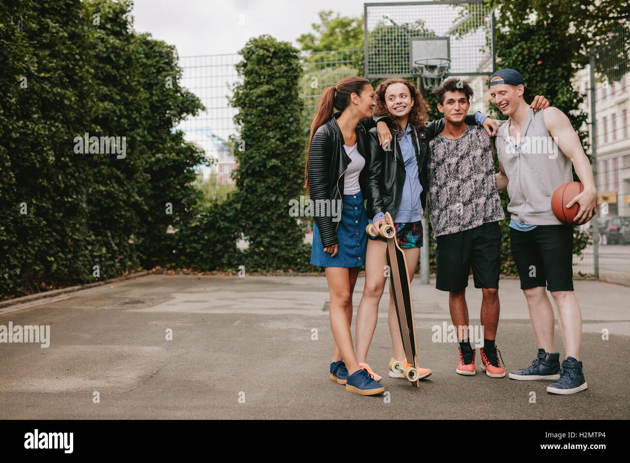 Full length portrait of teenage friends standing together with skateboard and basketball. Mixed race group of people enjoying ou Stock Photo
