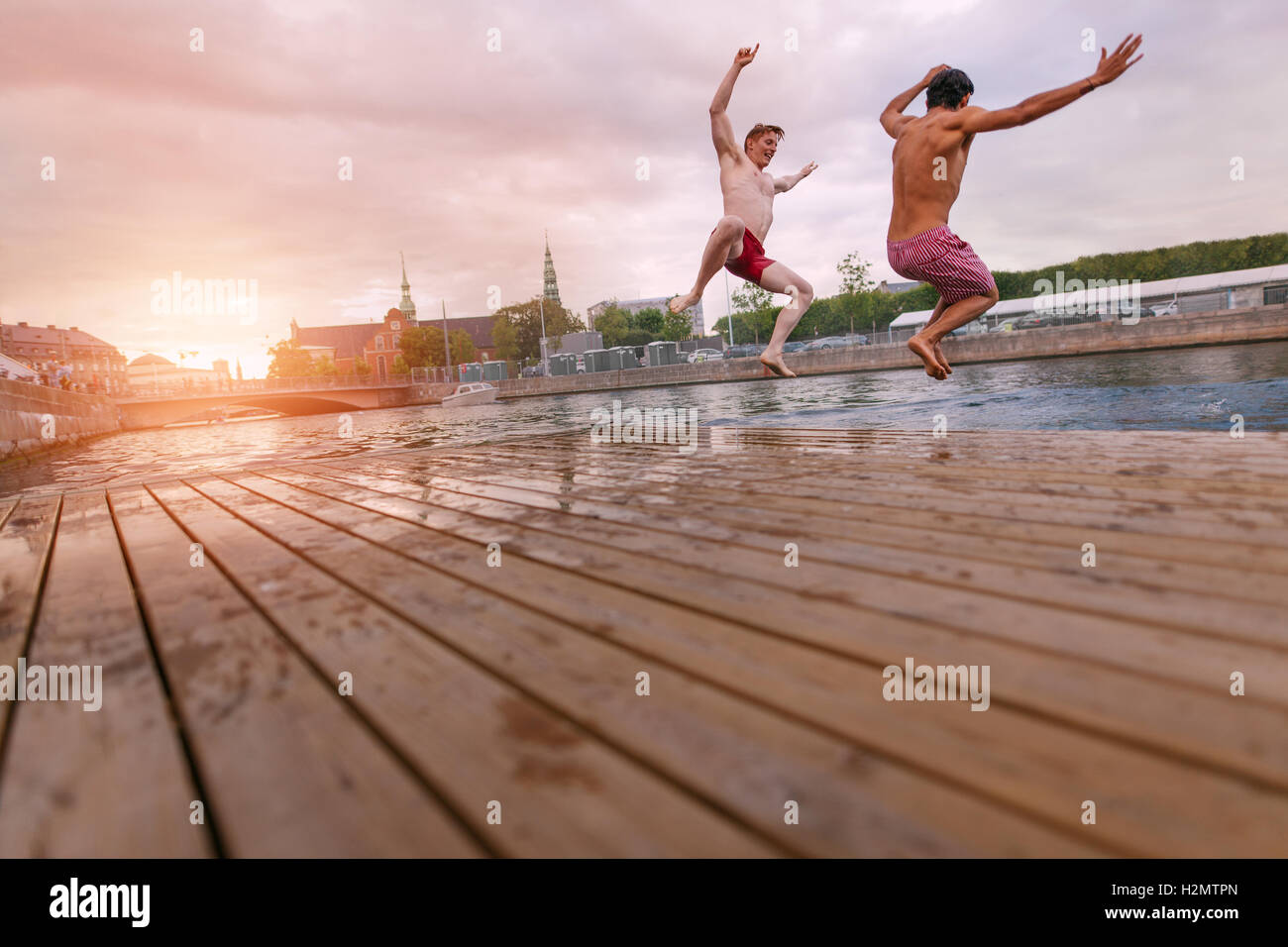Young people jumping into lake in city. Two young friends enjoying a weekend. Stock Photo