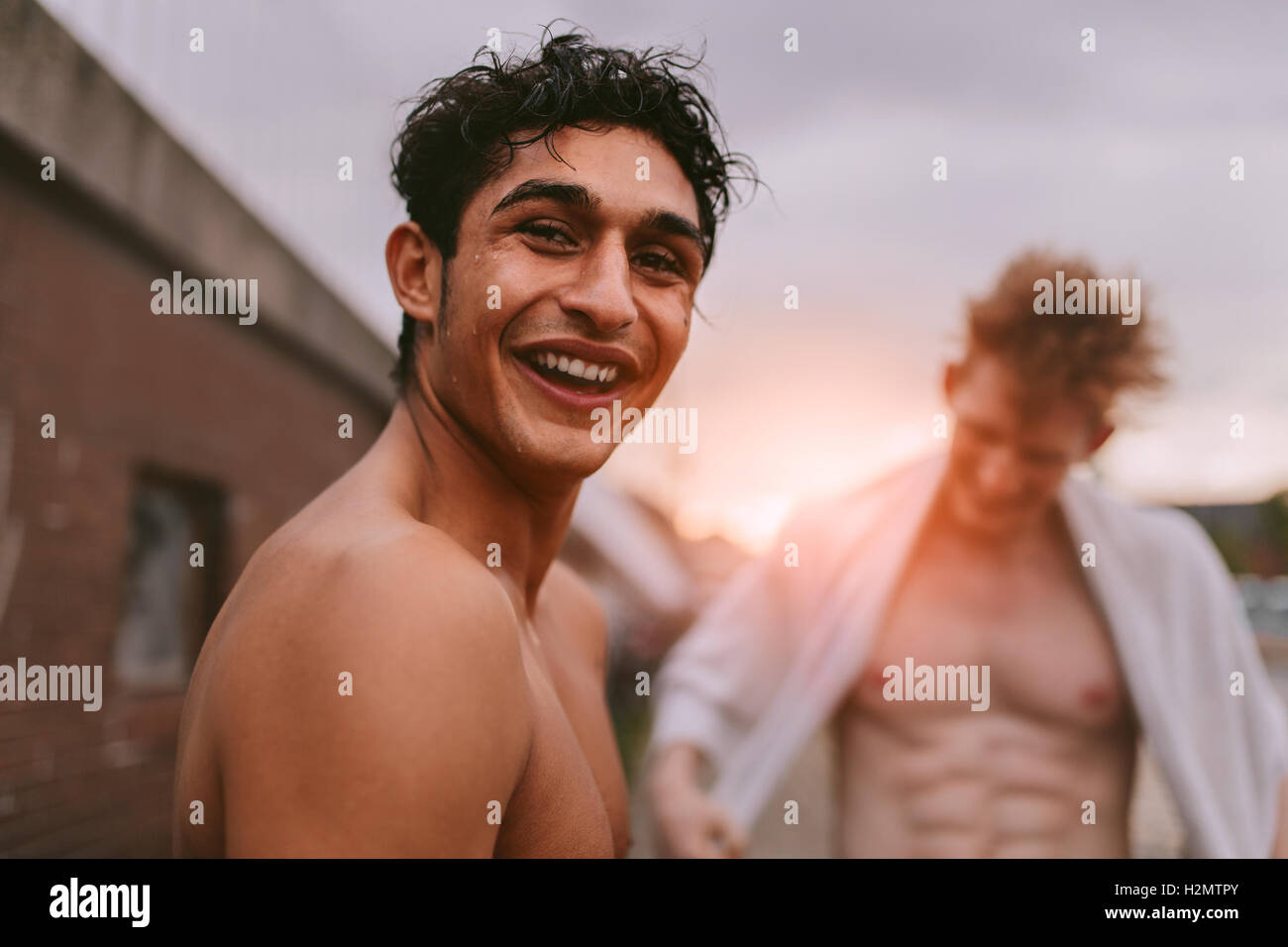 Portrait of handsome young man shirtless looking at camera and smiling with friends in background. Stock Photo