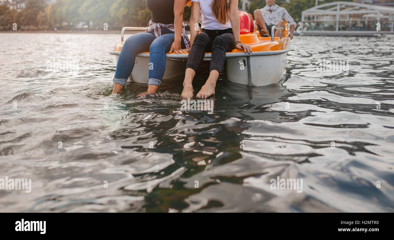 Cropped shot of young women sitting pedal boat front with feet in water. Two young women on a pedalo boat. Stock Photo