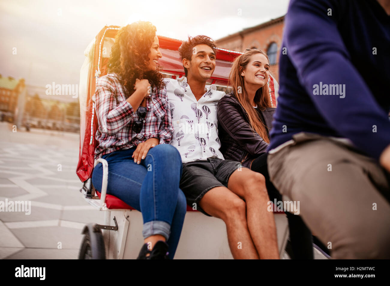 Group of young friends enjoying tricycle ride. Teenagers riding on tricycle on city road. Stock Photo