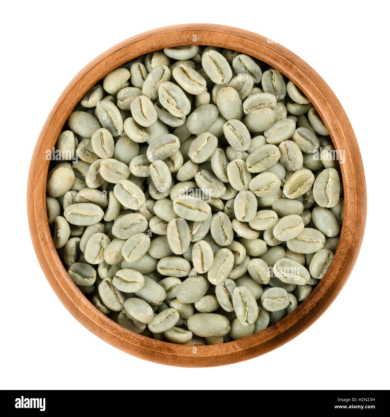 Green Arabica coffee beans in a wooden bowl on white background. Unroasted pits of the coffee cherries. Isolated close up macro. Stock Photo