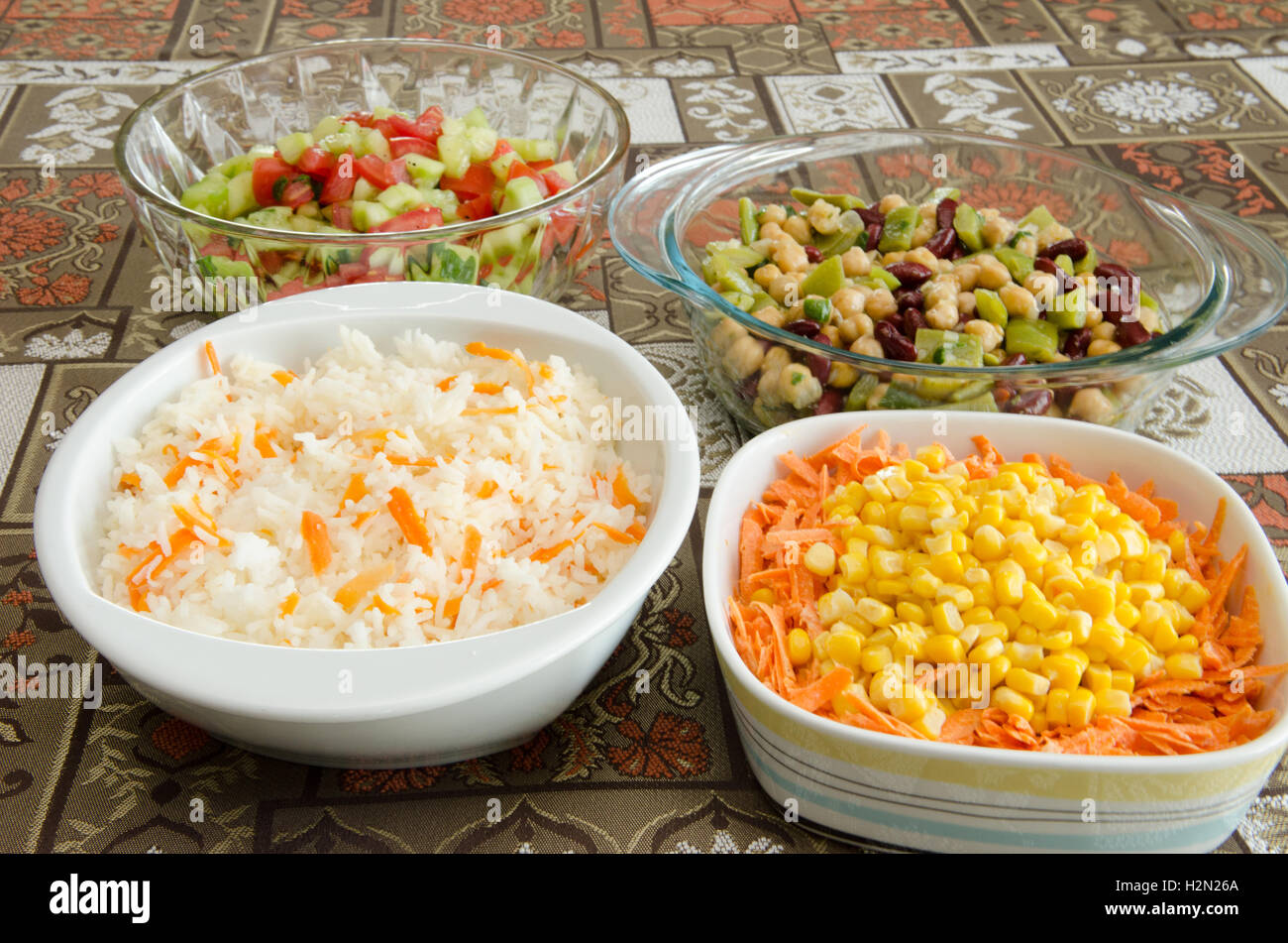 dishes of food items, steamed rice and carrots, three bean salad, corn and carrots and cucumber and tomato salad Stock Photo