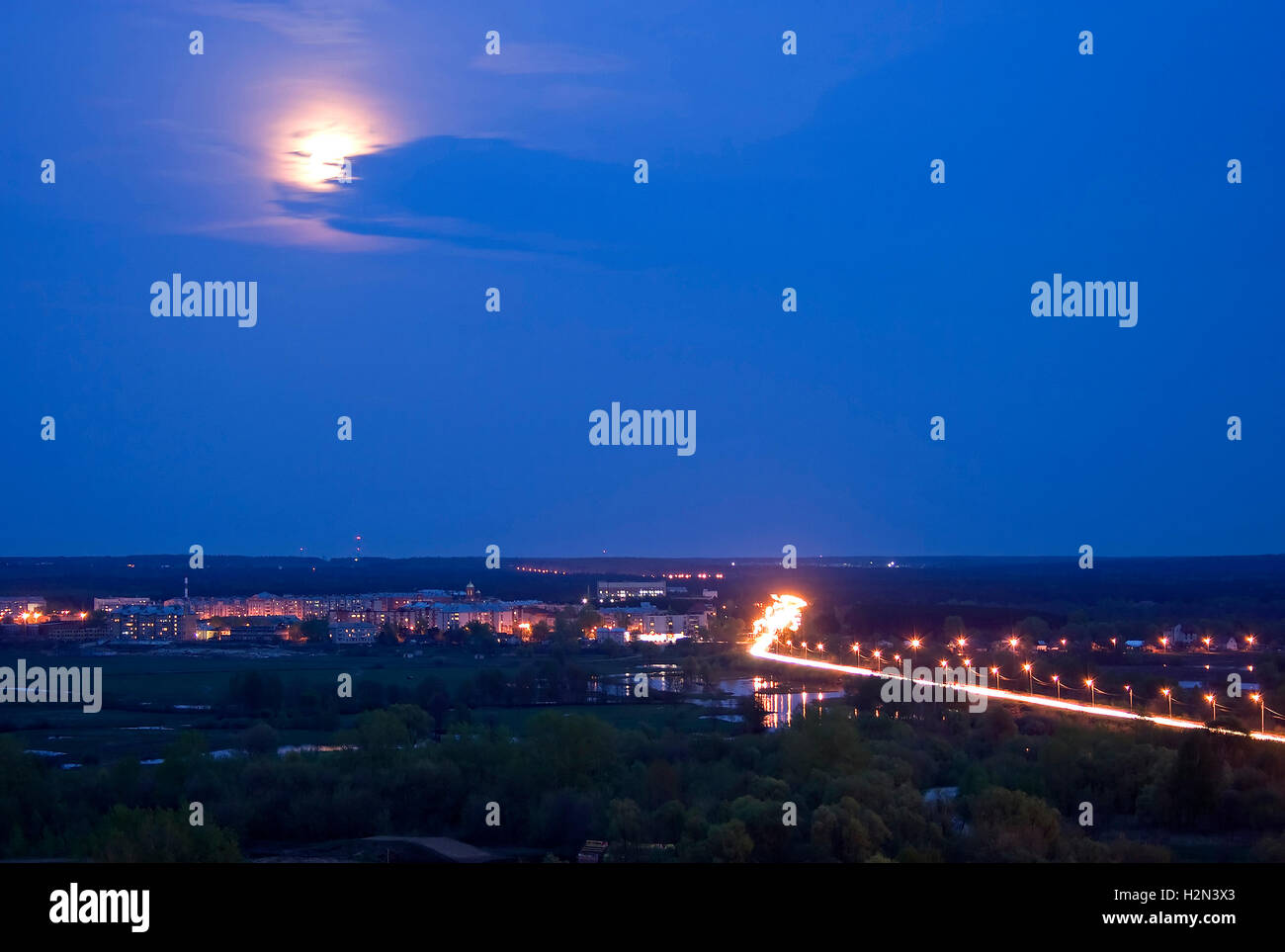 Night or evening russian landscape: river, road, bridge, lanterns, lamps, forest as a foreground; horizon, sky, clouds and Moon Stock Photo