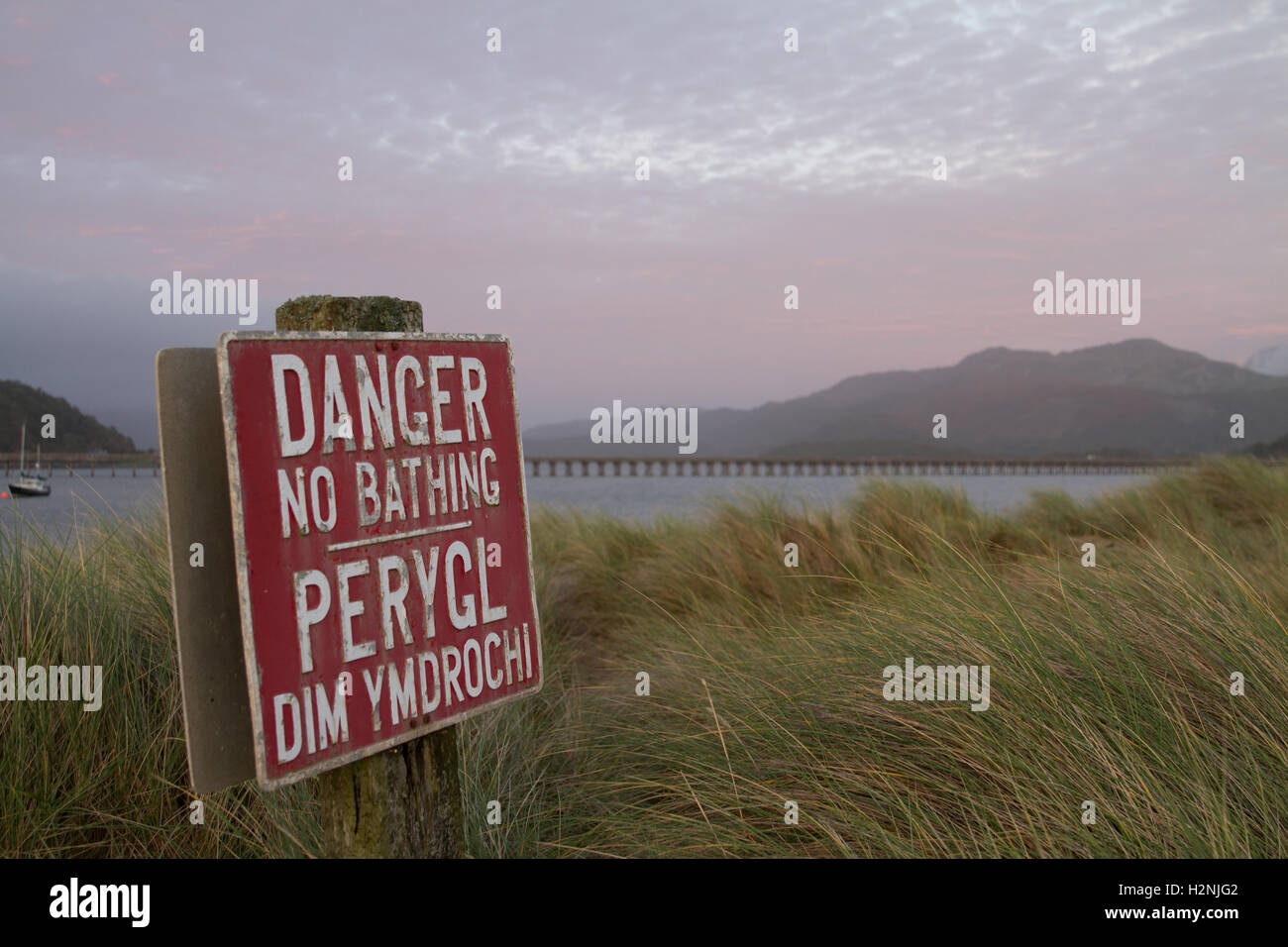 A bilingual sign warns would be bathers of the dangers of swimming in the Mawddach estuary, North Wales - Network Rail Barmouth Bridge wooden viaduct Stock Photo