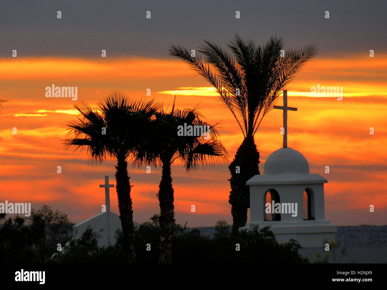 Palm tree next to church with two crosses at gold, orange, pink sunrise in Anza-Borrego Desert Stock Photo