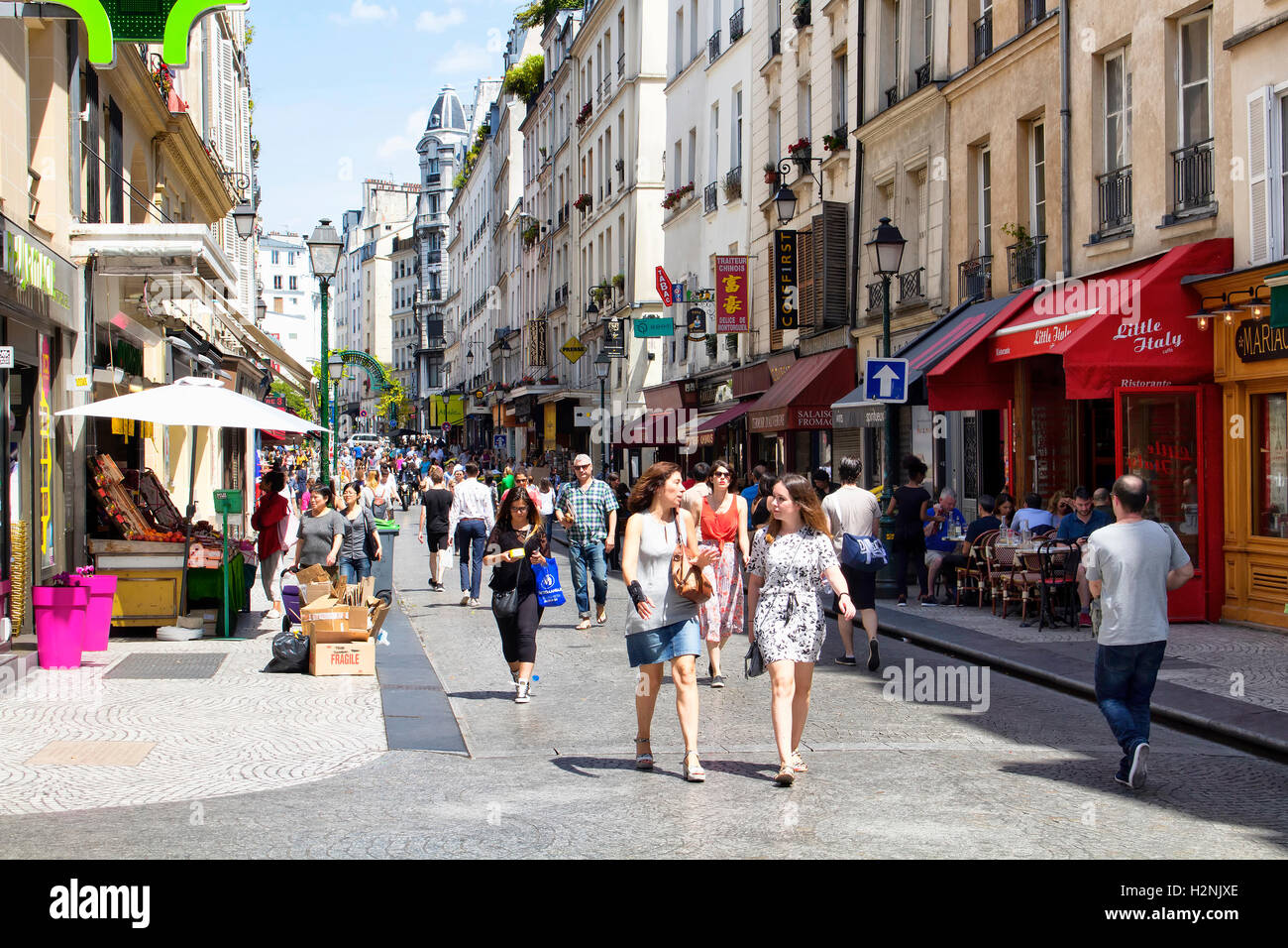 People walk on Rue Montorgueil street on sunny day in Paris. Cafes, little shops and French architecture style buildings are in Stock Photo