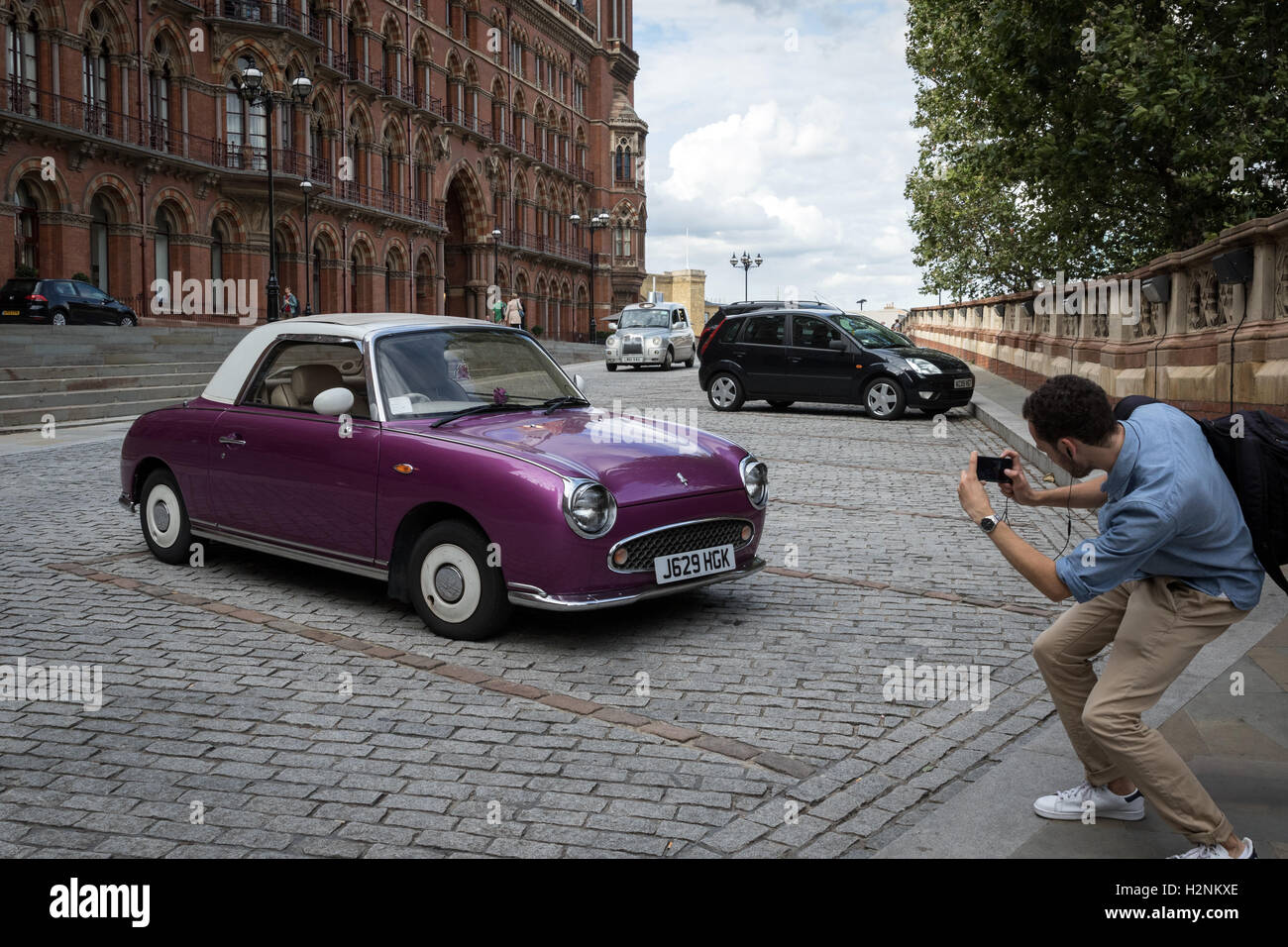 A passer-by takes a photograph of a Nissan Figaro car parked at St Pancras railway station and hotel in north London Stock Photo