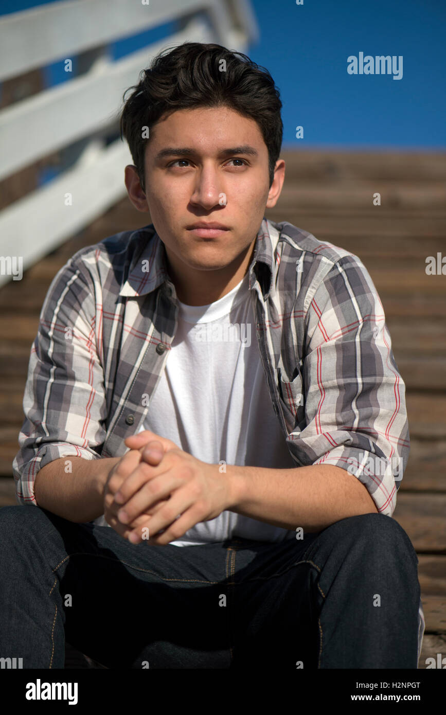 Young teenage male sitting on steps outdoors, looking off into the distance; thinking, pensive Stock Photo