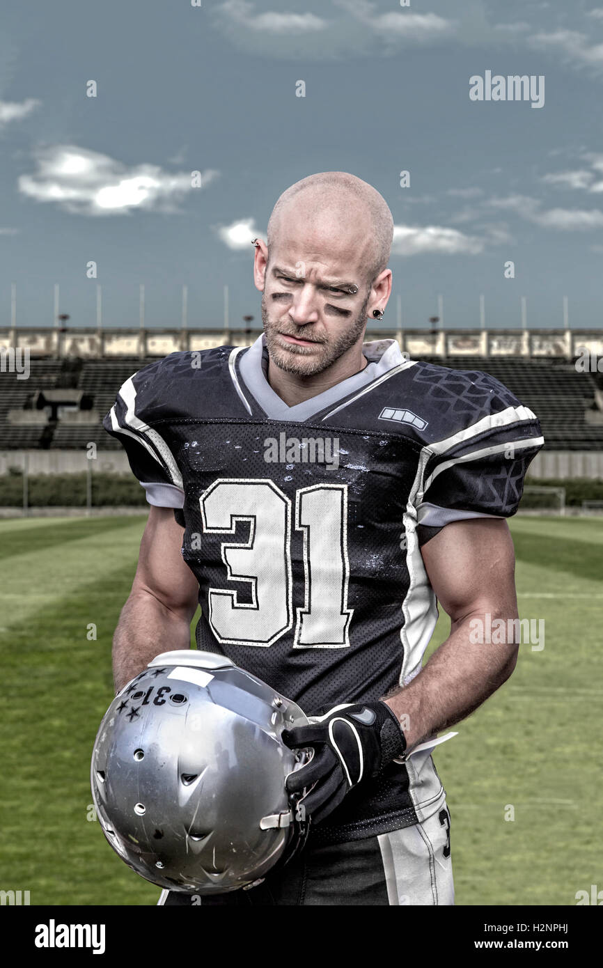 Portrait of a serious looking american football player, who stands alone in a desolate stadium. Stock Photo
