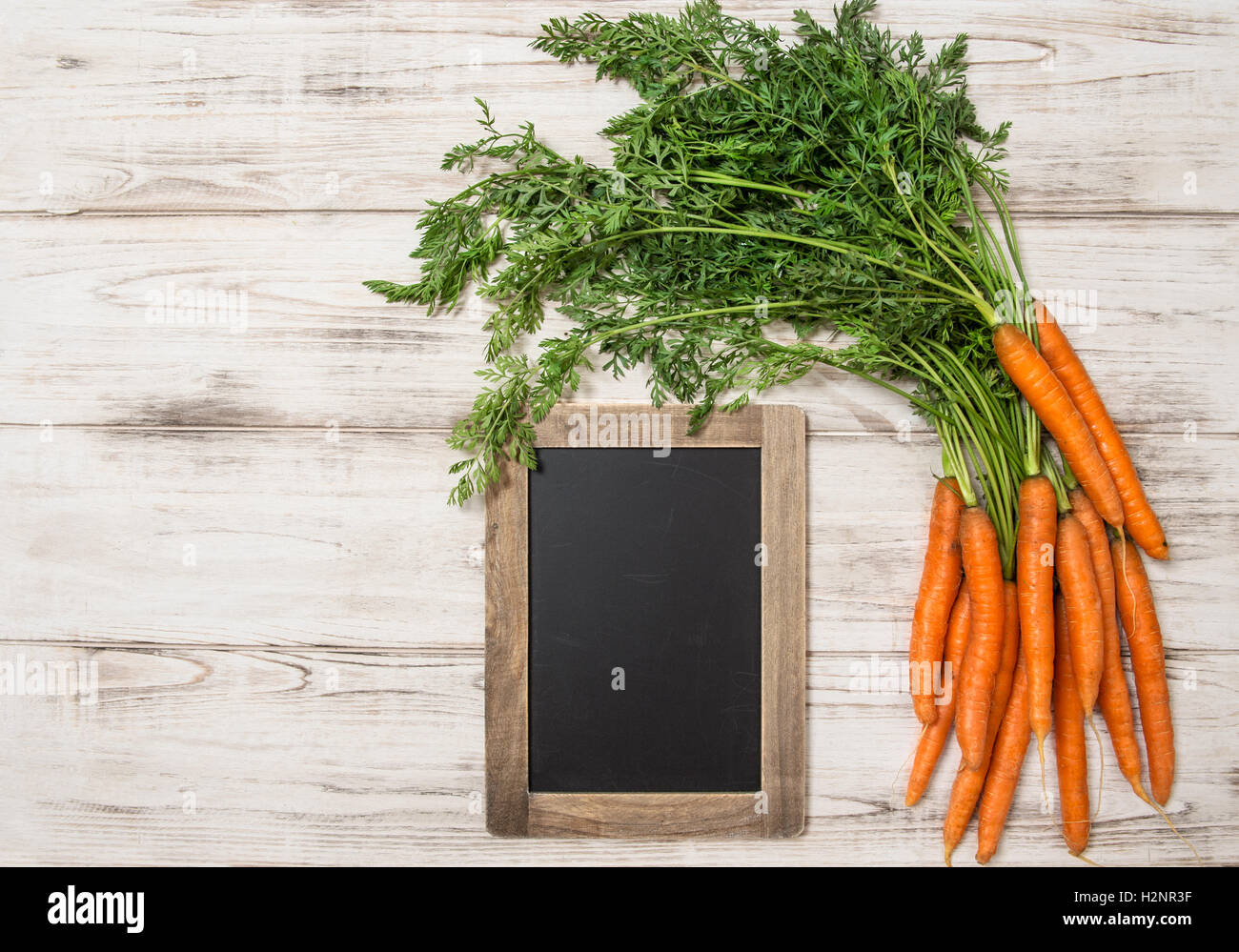 Fresh carrots roots with green leaves and blackboard over wooden background. Organic food concept Stock Photo