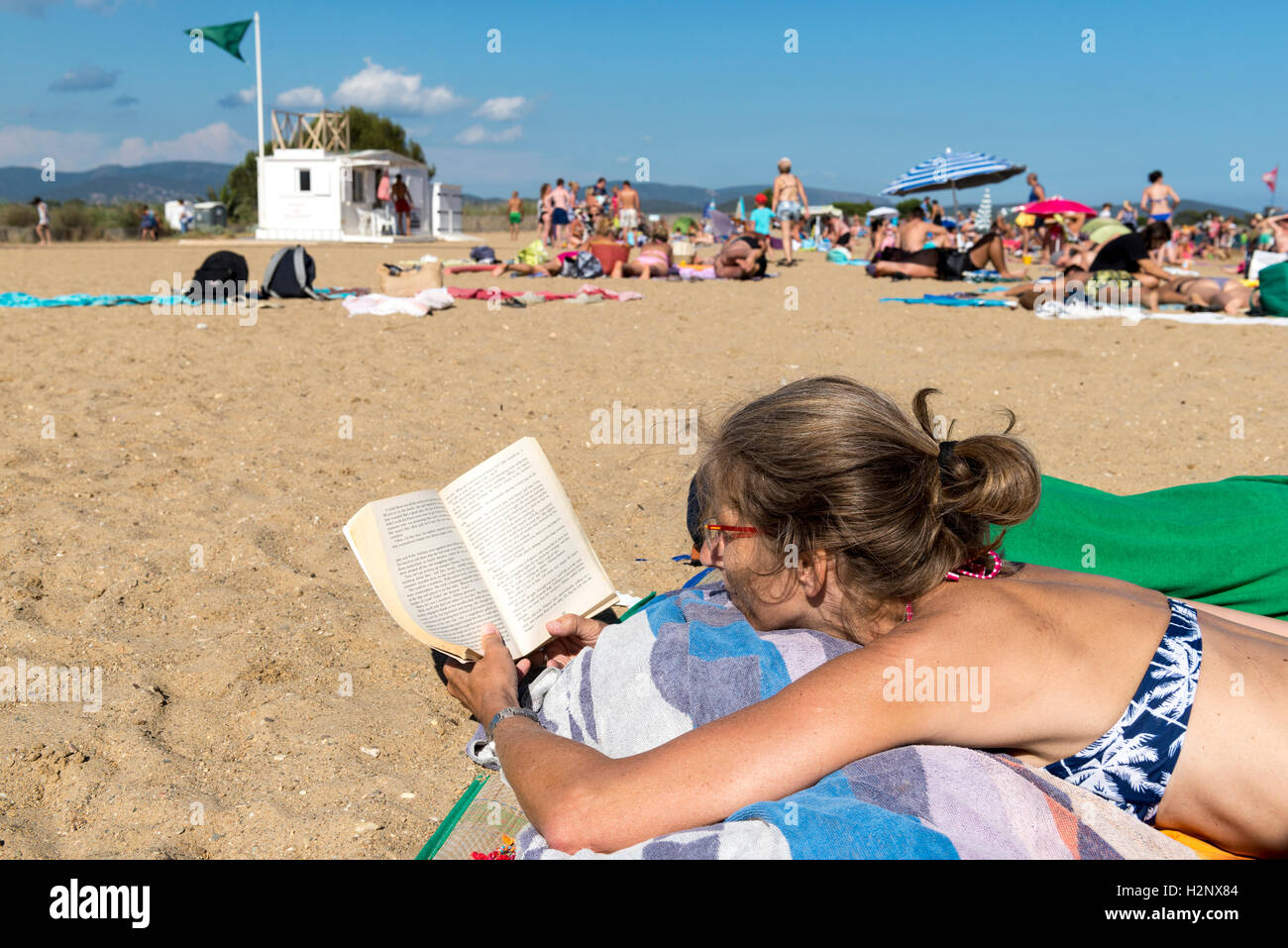 Woman lying on the beach reading a book, closeup, Plage des Salins, Hyeres, Côte d'Azur, France Stock Photo