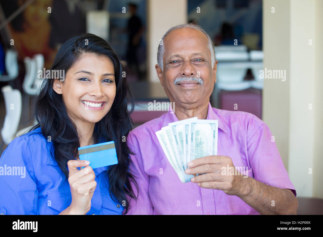 Closeup portrait rich elderly gentleman in pink shirt and lady in blue top holding greenbacks and credit card. Booming economy Stock Photo