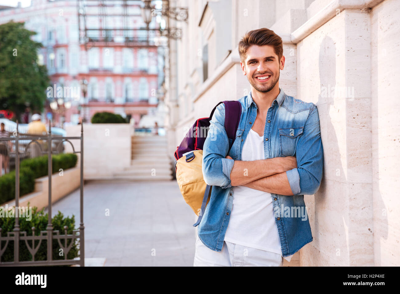Portrait of a smiling casual man with backpack and arms folded standing ...
