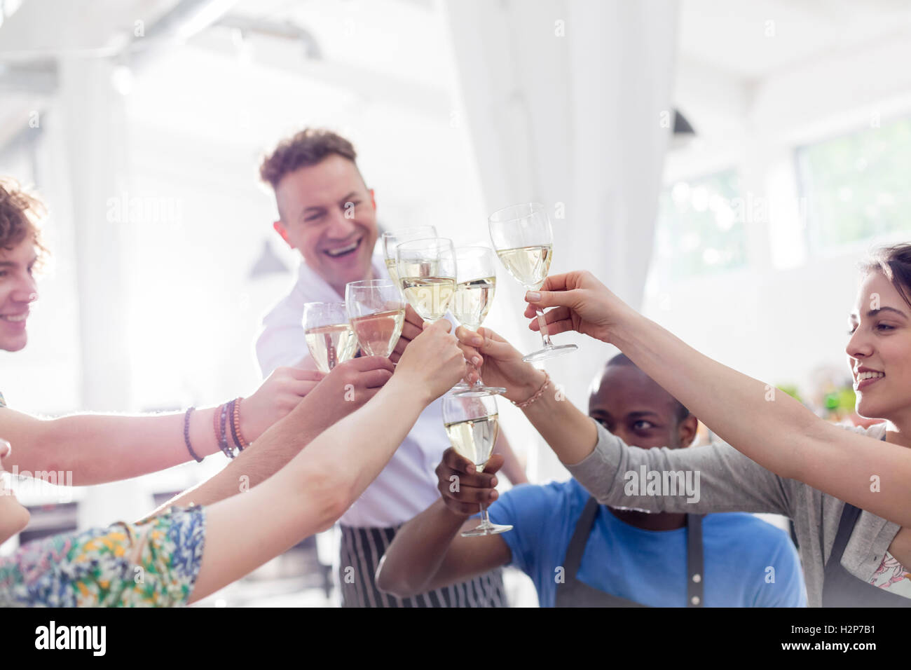Chef teacher and students toasting wine glasses in cooking class kitchen Stock Photo