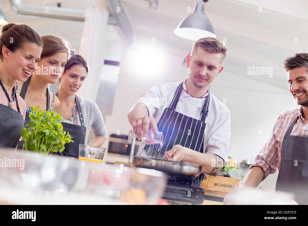 Students watching chef teacher at frying pan in cooking class kitchen Stock Photo