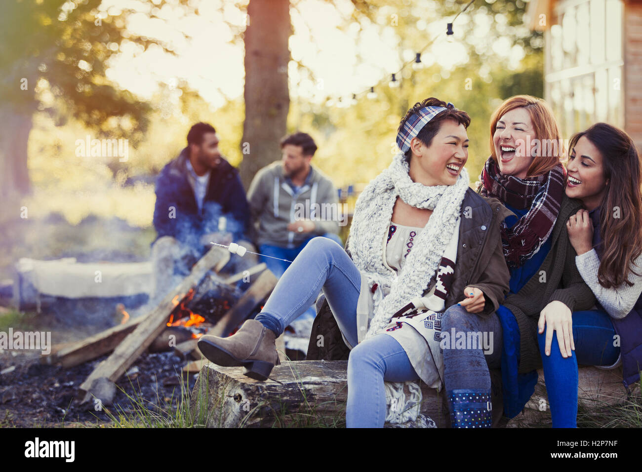 Female friends laughing and roasting marshmallows at campfire Stock Photo