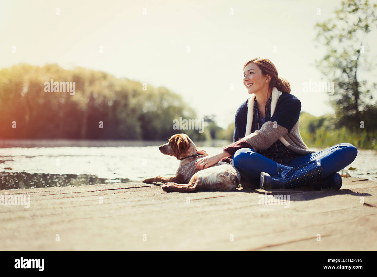 Smiling woman and dog relaxing on sunny lakeside dock Stock Photo