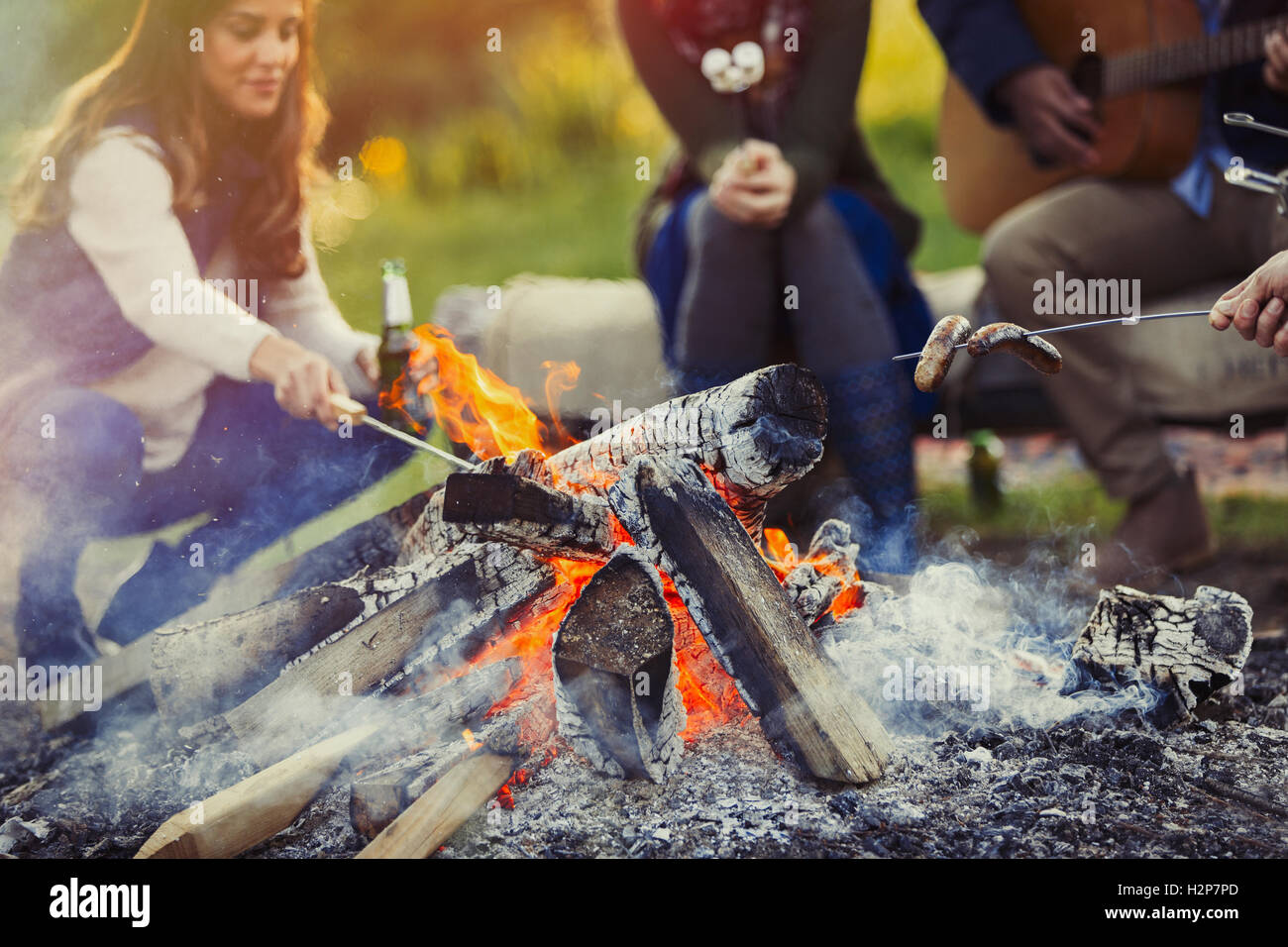Friends cooking hot dogs and drinking beer at campfire Stock Photo