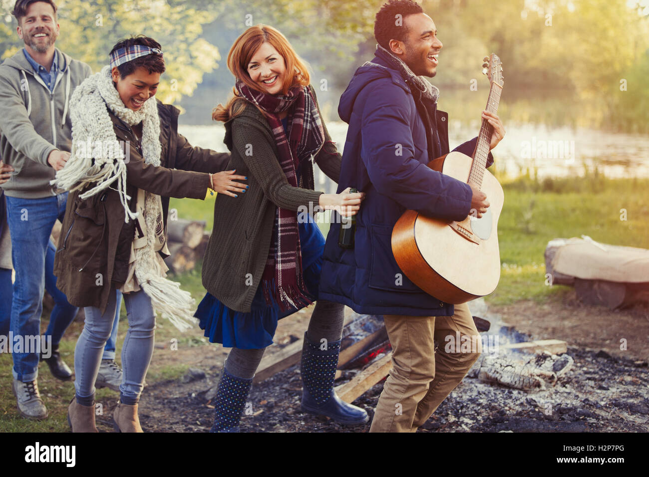 Playful friends with guitar dancing in conga line at campsite Stock Photo