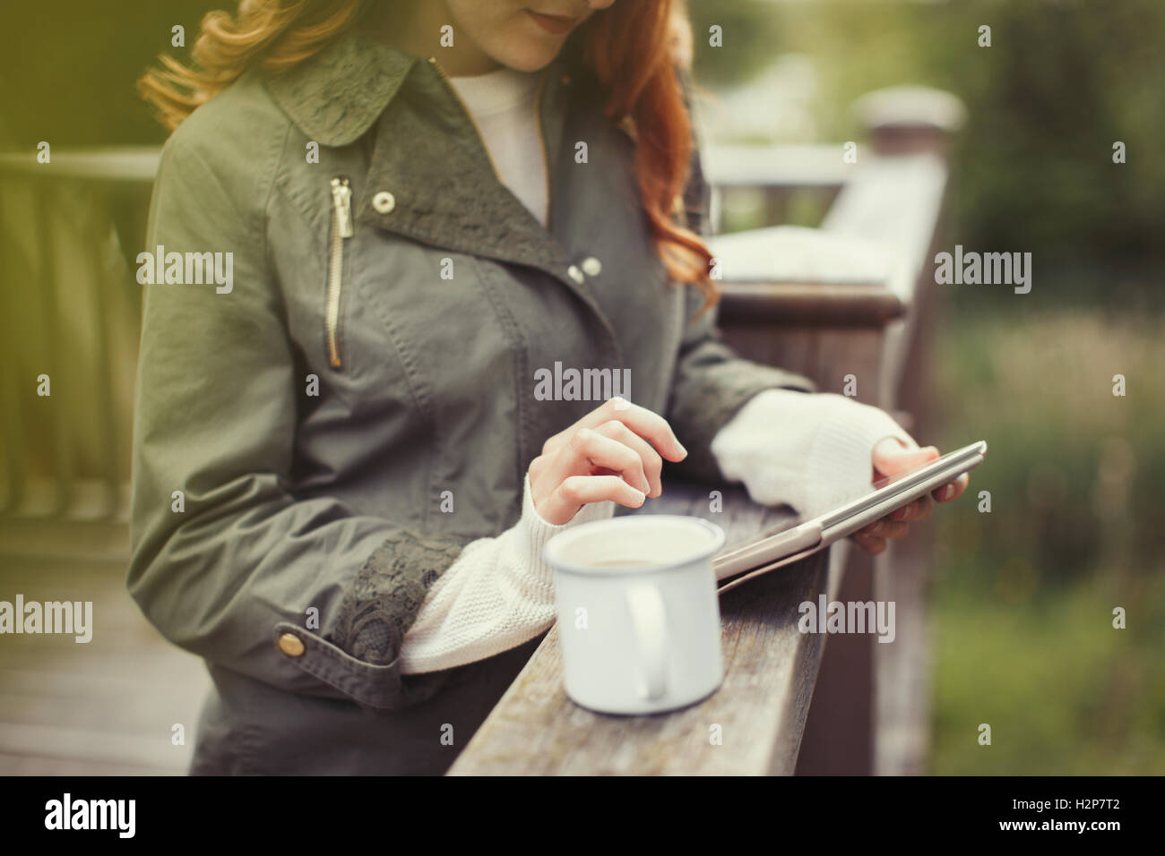 Woman drinking coffee using digital tablet at balcony railing Stock Photo