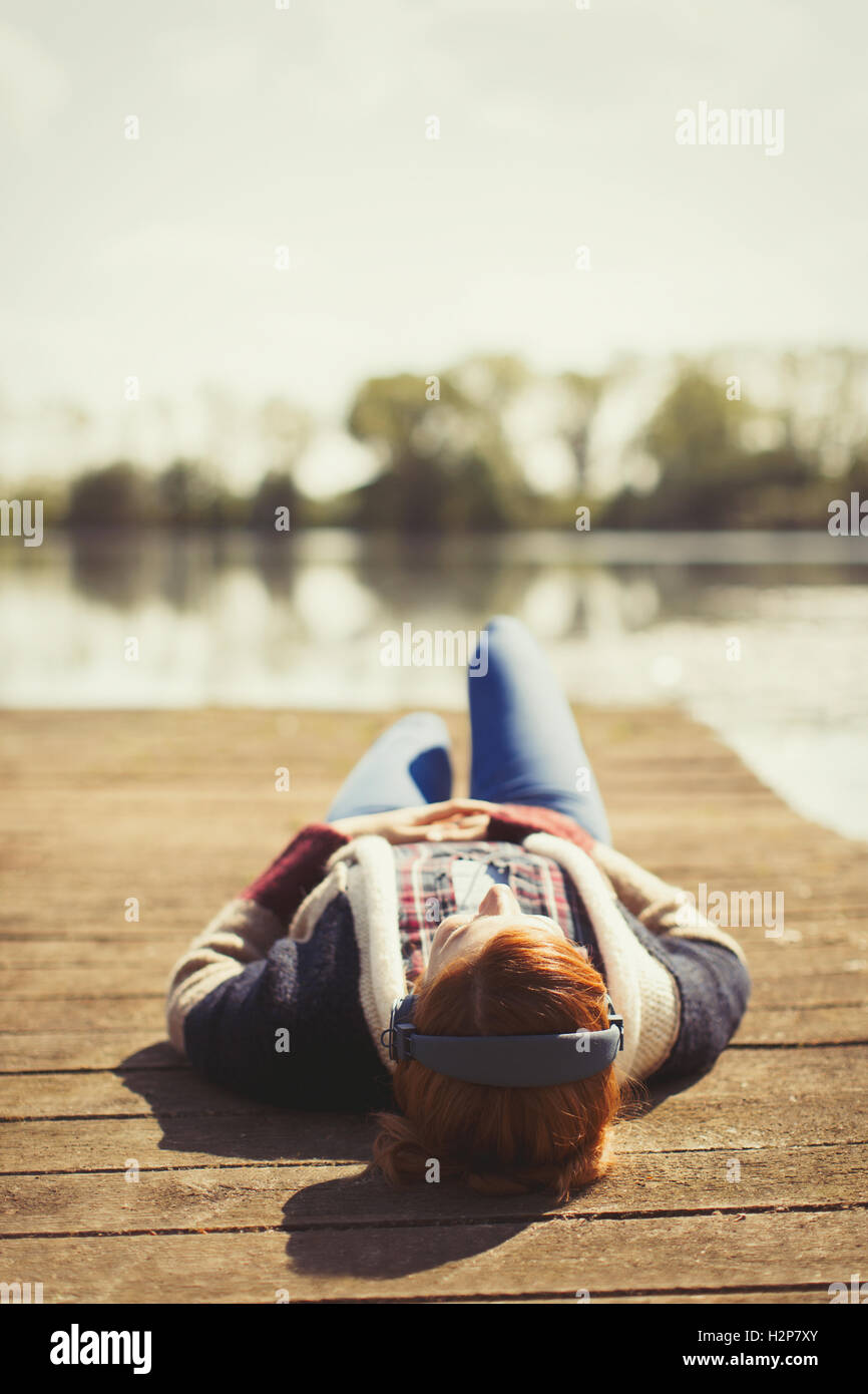 Woman laying relaxing listening to music with headphones on sunny lakeside dock Stock Photo