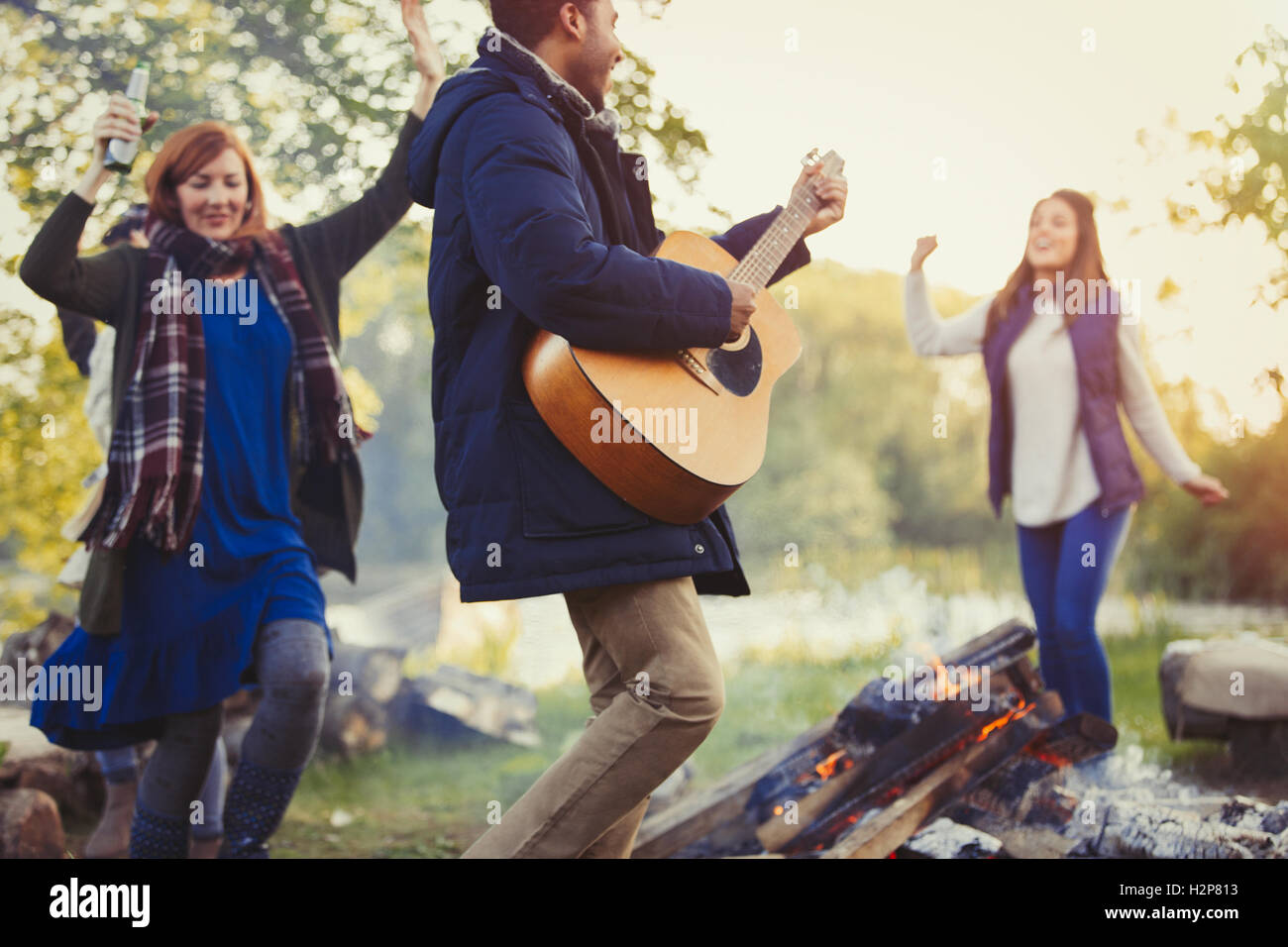Friends dancing and playing guitar around campfire Stock Photo